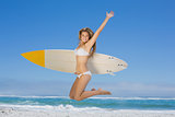 Smiling surfer girl holding her surfboard and jumping on the beach