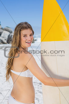 Fit smiling surfer girl holding her surfboard on the beach