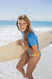 Fit smiling surfer girl on the beach with her surfboard