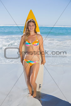 Beautiful smiling surfer girl standing on the beach with her surfboard