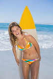 Beautiful smiling surfer girl standing on the beach with her surfboard