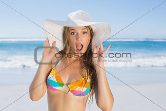 Beautiful girl in bikini and straw hat looking at camera on beach
