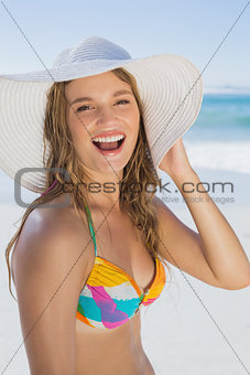 Beautiful girl in bikini and straw hat smiling at camera on beach