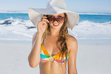 Beautiful girl in bikini and straw hat smiling at camera on beach