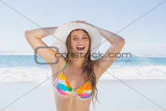 Beautiful girl on the beach smiling in white straw hat and bikini