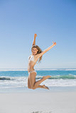 Fit smiling woman in white bikini leaping on beach