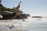 Beautiful smiling woman in white bikini leaping on the beach