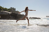 Beautiful smiling woman in white bikini leaping on the beach