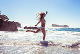 Beautiful smiling woman in white bikini skipping on the beach