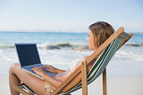 Woman relaxing in deck chair on the beach using laptop