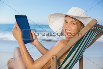Smiling woman relaxing in deck chair on the beach using tablet