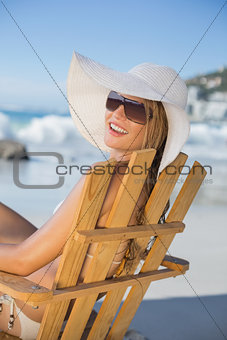 Smiling woman in straw hat relaxing in deck chair on the beach