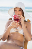 Pretty blonde relaxing in deck chair on the beach with cocktail