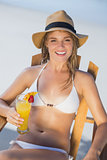 Pretty smiling blonde relaxing in deck chair on the beach with cocktail