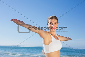 Sporty blonde standing on the beach with arms out