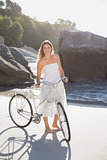 Beautiful blonde in white sundress standing with bike on the beach