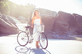 Beautiful blonde in white sundress standing with bike on the beach