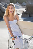 Beautiful surfer in sundress on bike holding surfboard at the beach