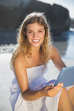 Beautiful smiling blonde in sundress using tablet on the beach