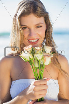 Beautiful blonde in sundress holding roses on the beach
