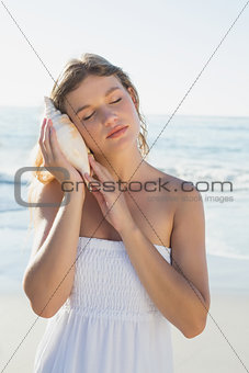 Beautiful blonde in white sundress on the beach listening to conch