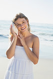 Beautiful blonde in white sundress on the beach listening to conch