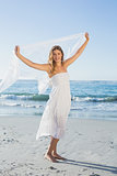 Beautiful happy blonde in white sundress on the beach with scarf