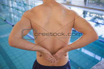 Fit swimmer touching his back by the pool