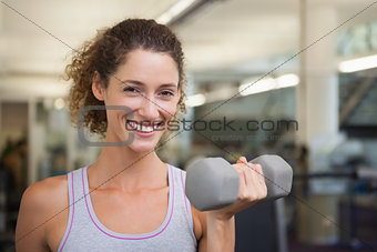 Fit woman smiling at camera lifting dumbbell