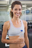 Fit woman smiling at camera holding water bottle
