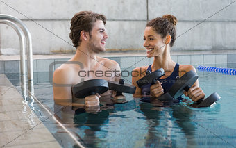 Man and woman standing with foam dumbbells in the pool