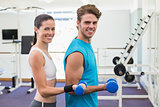 Fit couple exercising with blue dumbbells smiling at camera