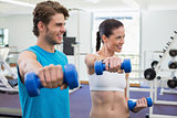 Fit couple exercising with blue dumbbells and smiling