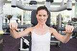 Fit brunette smiling at camera using weights machine for arms