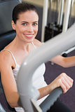 Fit brunette using weights machine for arms smiling at camera