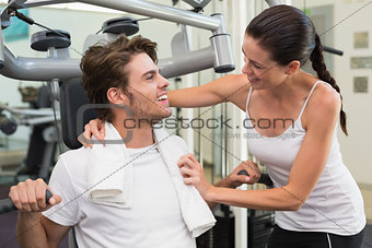 Fit man using weights machine with trainer encouraging him
