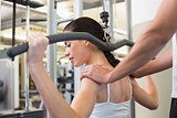 Fit brunette using weights machine for arms with trainer touching shoulders