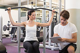 Fit brunette using weights machine for arms with trainer taking notes