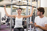 Fit brunette using weights machine for arms with trainer taking notes