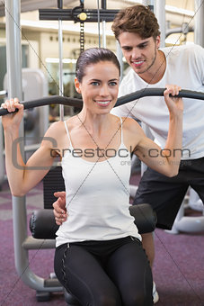 Fit brunette using weights machine for arms with trainer helping