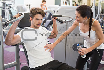 Fit man using weights machine for arms with his trainer