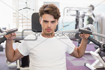 Fit man using weights machine for arms looking at camera