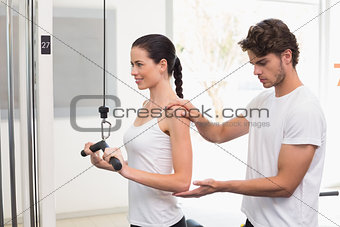 Fit smiling woman using weights machine for arms with her trainer