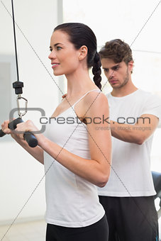 Fit smiling woman using weights machine for arms with her trainer