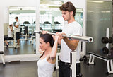 Fit woman lifting barbell with her trainer spotting