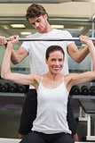 Fit smiling woman lifting barbell with her trainer spotting
