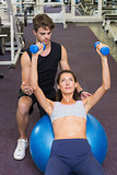 Trainer watching client lying on exercise ball with dumbbells