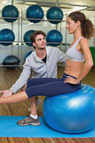 Trainer watching his client lift leg on exercise ball