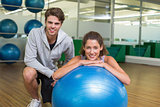 Fit woman leaning on exercise ball with trainer smiling at camera