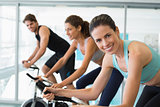 Fit people in a spin class with brunette smiling at camera